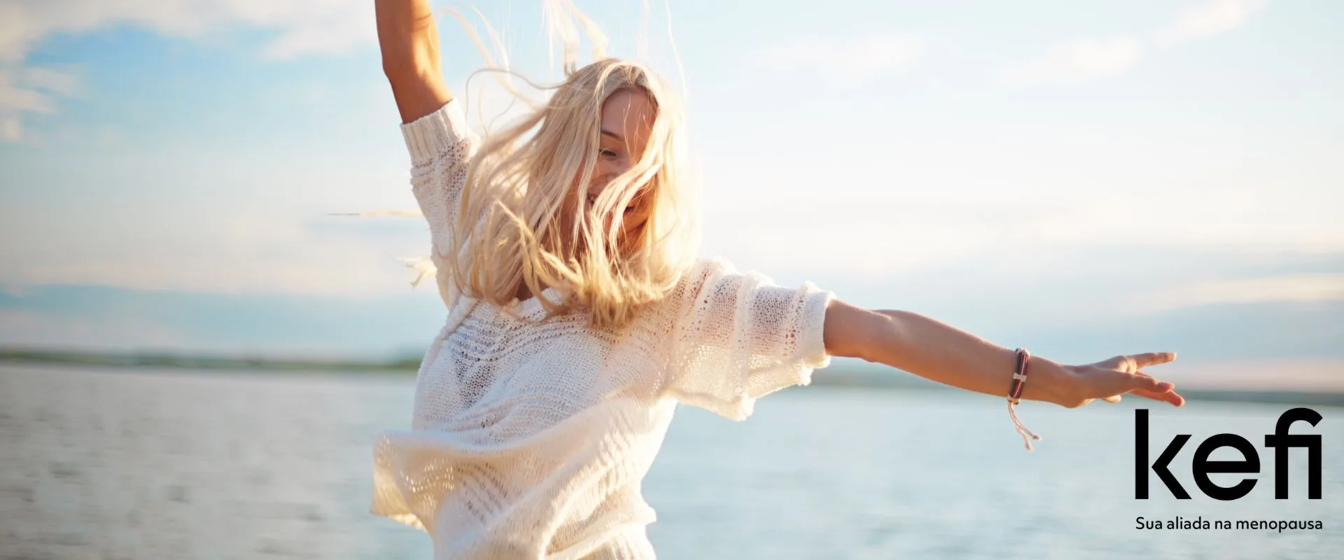 Mulher feliz estendendo os braços para o céu aberto, simbolizando liberdade e bem-estar durante o climatério, representando a alegria e o autoconhecimento na menopausa, com a logo da Kefi, sua aliada nesta jornada.