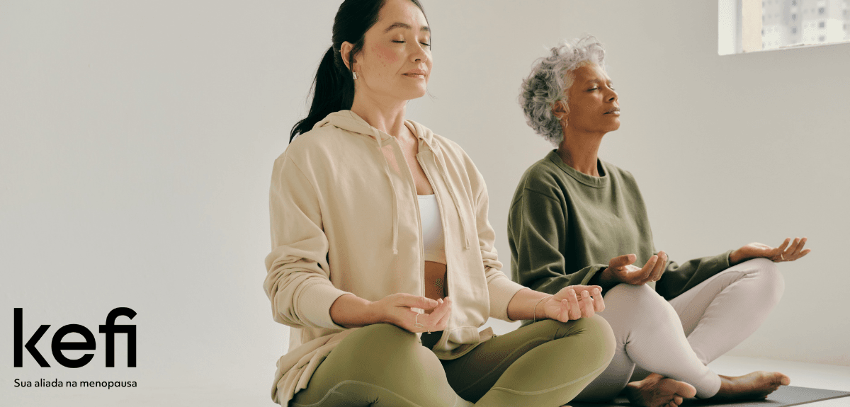 Duas mulheres em idade madura praticando meditação em uma sala iluminada, simbolizando os benefícios da meditação na menopausa para a saúde mental e emocional.
