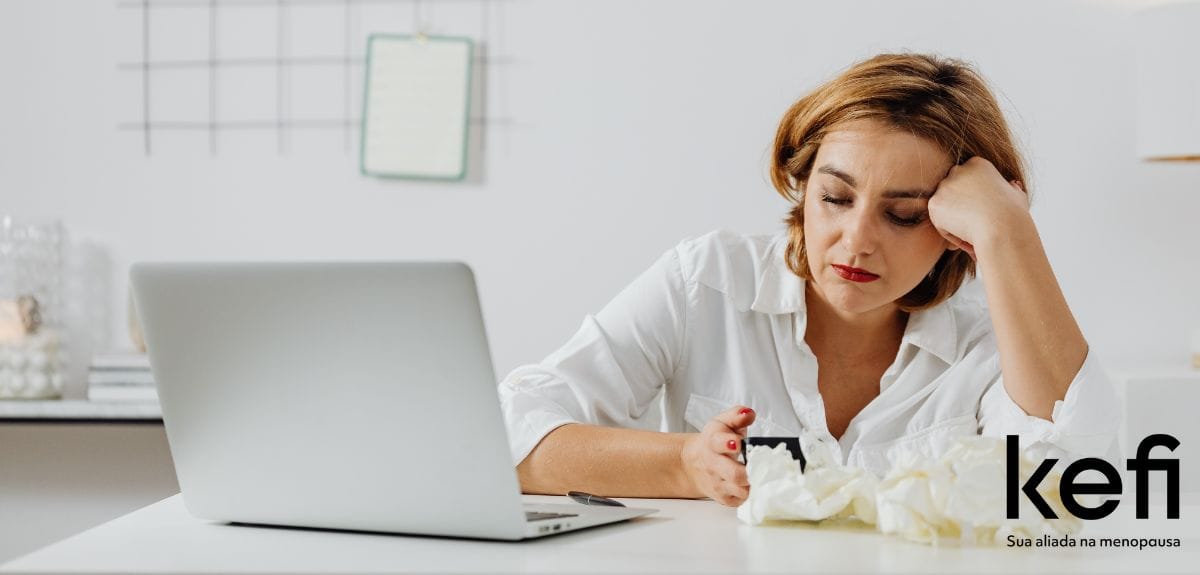 Mulher exausta sentada em frente ao computador, com expressão de cansaço e desânimo, representando os impactos da insônia na saúde feminina e no dia a dia.